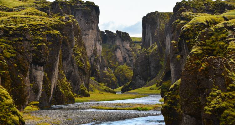 Dramatische, moosbedeckte Canyonwände mit einem sich windenden Fluss am Grund unter bedecktem Himmel.