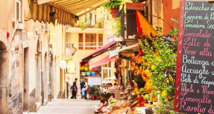 Charmante enge italienische Gasse mit farbenfrohem Gemüse, Schildern und Cafè-Markisen