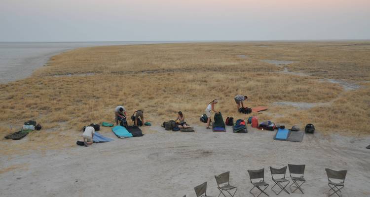 Groupe de personnes installant du matériel de camping dans un paysage ouvert et aride au crépuscule.