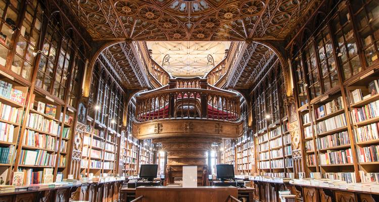 Interior ornamentado de la librería Livraria Lello con una majestuosa escalera y un techo de madera detallado.