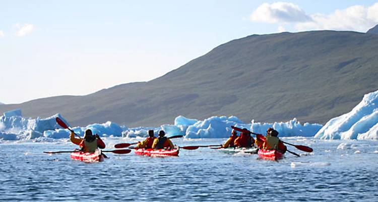 Group of people kayaking near icebergs in a cold, scenic setting.