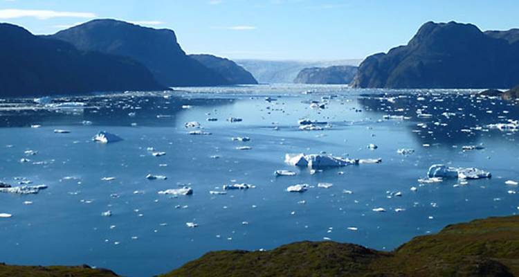 Wide view of a fjord with icebergs and mountains in the background.