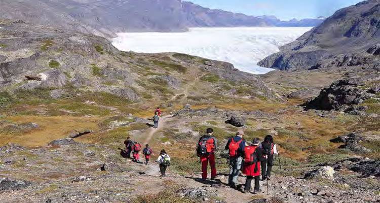 Hikers on a trail with icy mountain glacier in the distance.