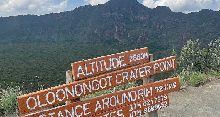Schild, das zum Oloonongot-Kraterpunkt zeigt, mit Bergen im Hintergrund.