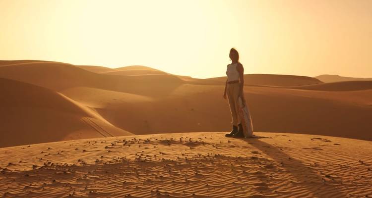 Person, die bei Sonnenuntergang auf einer Sanddüne steht.