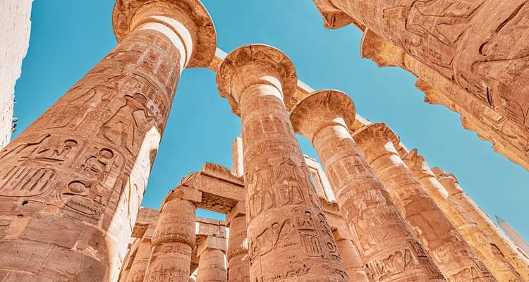 Massive ancient columns with hieroglyphs against a blue sky.