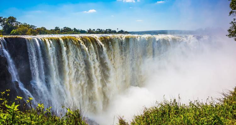 Brede gordijn van de Victoria Falls die op een zonnige dag in een mistige afgrond stort.