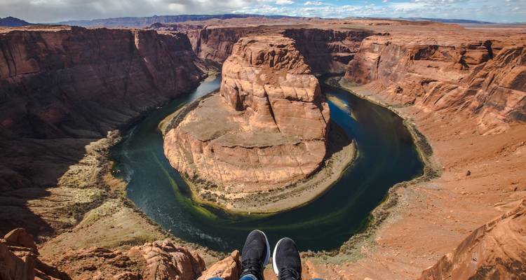 Horseshoe Bend viewpoint with traveler’s feet dangling above the winding Colorado River.