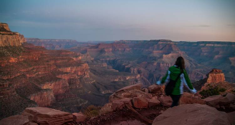 Twilight view over the Grand Canyon with blurred traveler standing on rocky edge.