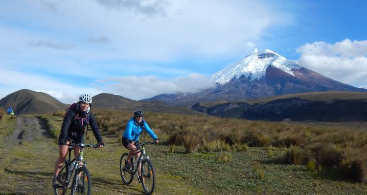 Deux cyclistes roulant devant une montagne enneigée, probablement le Cotopaxi.
