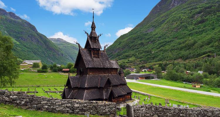 Medieval wooden Borgund Stave Church nestled in lush Norwegian valley with mountains behind.