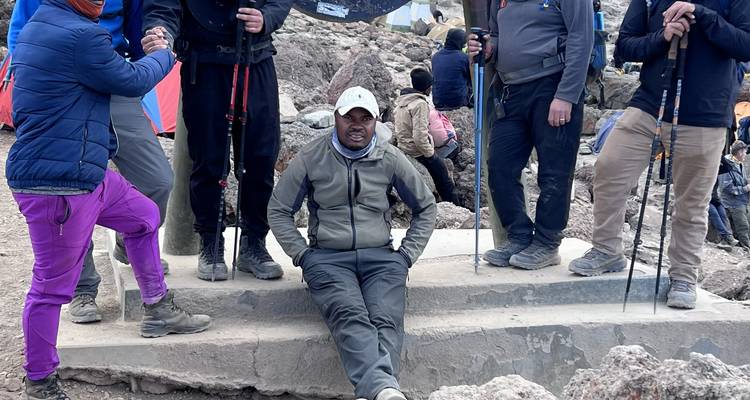 Trekkinggruppe ruht sich auf felsigen Stufen mit Wanderstöcken in einem Hochlagercamp aus.