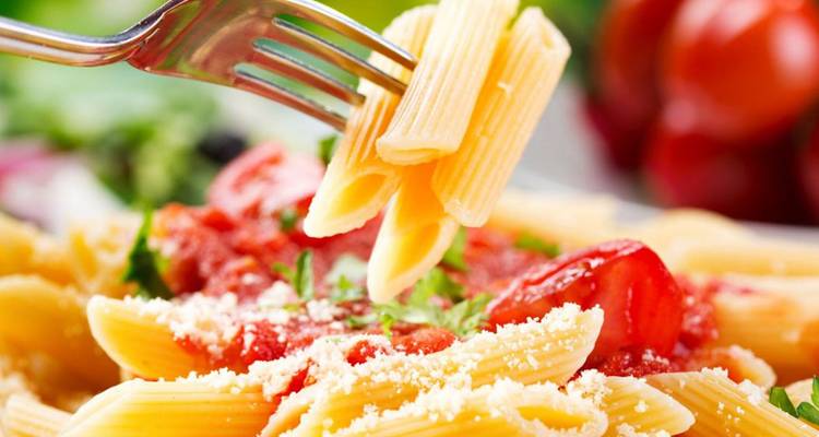 Close-up of pasta with sauce and tomatoes on a fork.