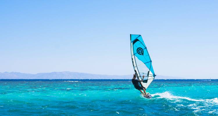 Persona haciendo windsurf en agua turquesa.