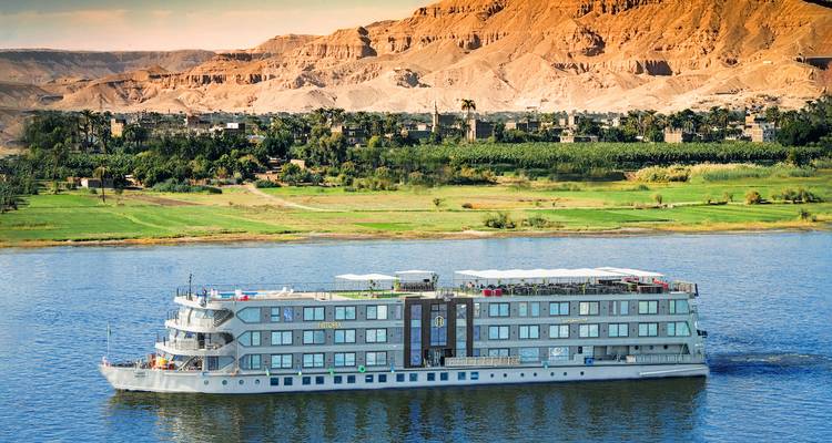 Cruise ship sailing on a river with mountains in the background.