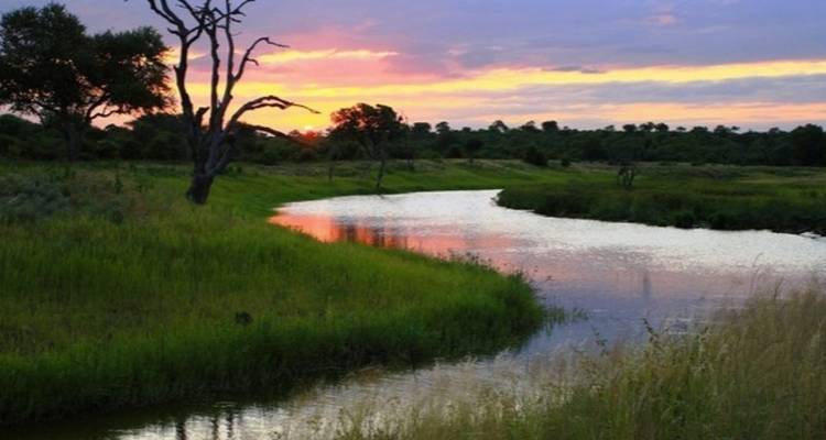 Calm river reflecting a colorful sunset in a grassy landscape.