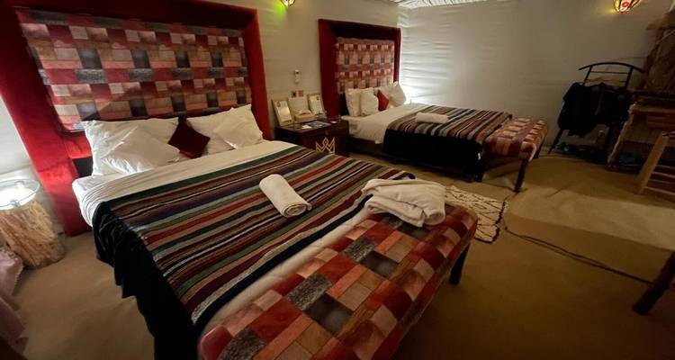 Acogedora habitación de campamento desértico con dos camas a rayas coloridas, alfombras e iluminación suave.