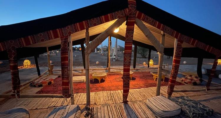 Interior de tienda bereber abierta con alfombras y cojines estampados iluminados suavemente bajo el cielo nocturno.