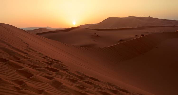 Las dunas de arena roja rodante brillan bajo el sol poniente en el Sahara.