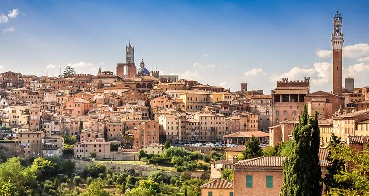Golden sunlight bathes a medieval hill city with distinctive towers and domes rising above rooftops.