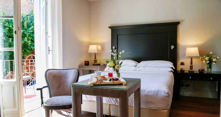 Bright hotel room with breakfast tray on a small table beside the neatly made bed.