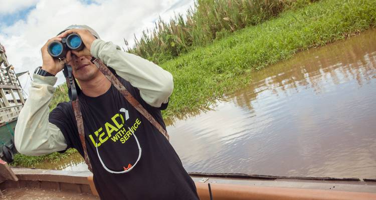 Ein Führer mit Fernglas beobachtet die Tierwelt am Flussufer von einem Holzboot aus im Amazonas.