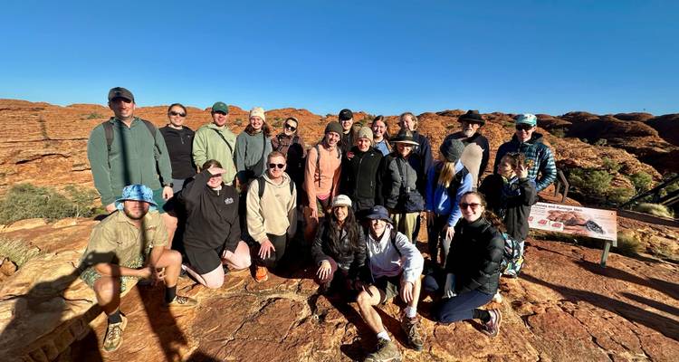 Groupe de personnes posant sur un paysage rocheux avec un panneau indicateur.