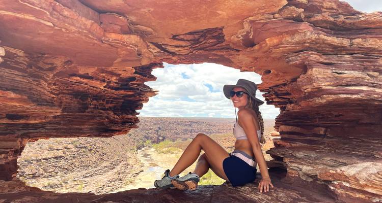 Mujer sonriente sentada en la ventana de roca natural con vista a un cañón desértico accidentado