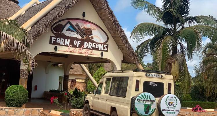Safari vehicle parked outside the thatched entrance of Farm of Dreams Lodge surrounded by tropical plants.