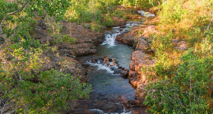Small cascading river flowing through rocky pools in lush Australian bush at golden hour.