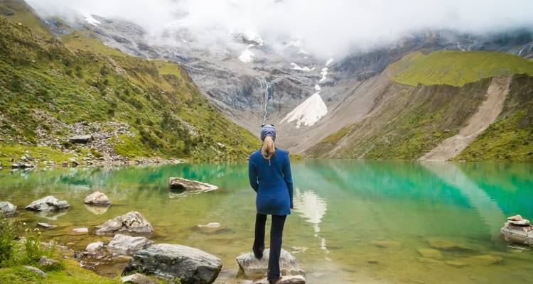 Femme regardant un lac turquoise avec un paysage de montagnes en arrière-plan.