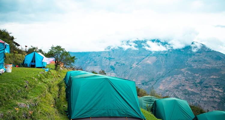 Tentes dressées sur une colline verdoyante avec un paysage montagneux en arrière-plan.