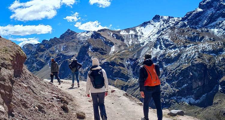 Des randonneurs marchant le long d'un sentier de montagne avec des pics enneigés dominant autour d'eux.