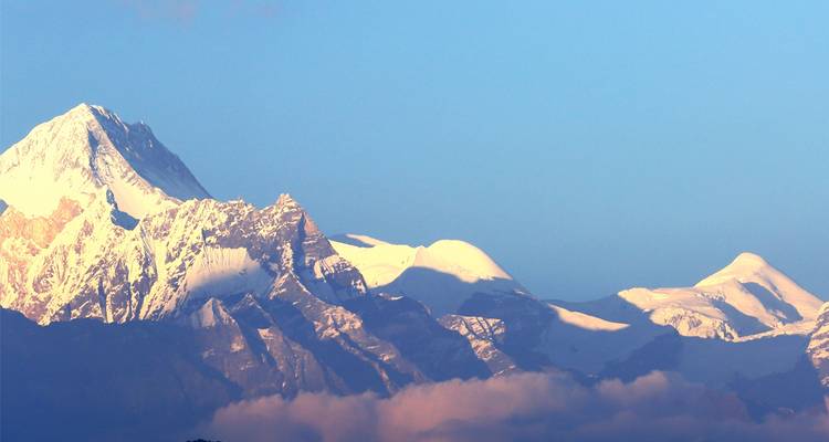 Primer plano de picos nevados del Himalaya iluminados por el sol contra un cielo azul claro encima de las nubes