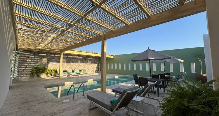 Elegante patio boutique con tumbonas junto a una piscina estrecha bajo un techo de pérgola con lamas.