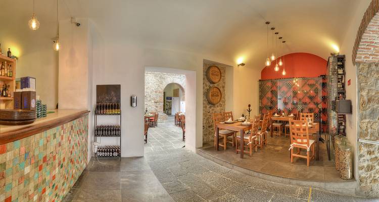 Interior de restaurante elegante con piso de piedra, mesas de madera, una barra con azulejos coloridos e iluminación cálida.