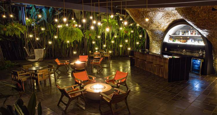 Bar lounge en plein air ambiant éclairé par des dizaines d'ampoules suspendues à côté de luxuriantes plantes tropicales.