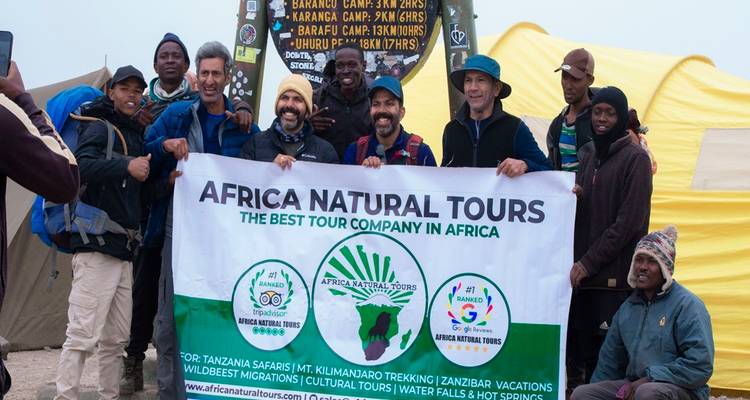 Large group of trekkers celebrating with banner at Mount Kilimanjaro trail sign