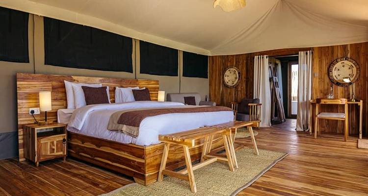 Ruim luxe safaritent interieur met houten meubels, kingsize bed en warm omgevingslicht op glanzende houten vloeren.