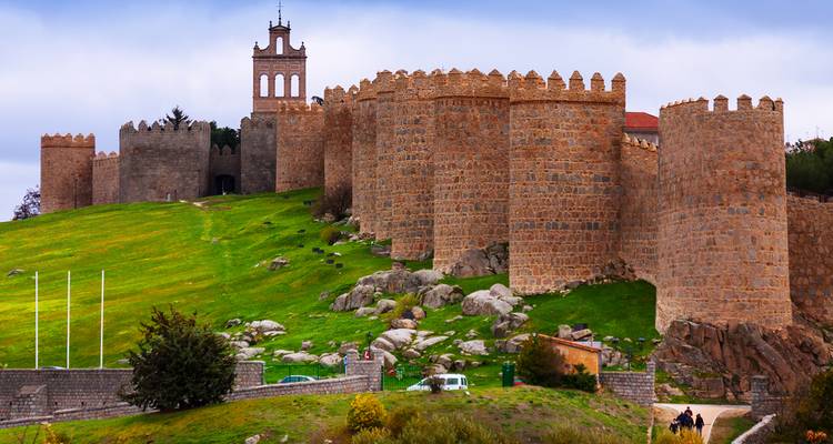 Historic city walls surrounding green hills in Ávila.