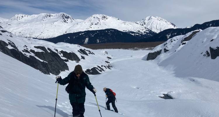 Wandelaars die een besneeuwde helling oplopen met uitzicht op bergen in de verte.