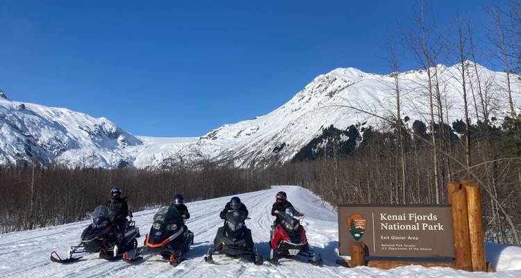 Sneeuwscooterchauffeurs die een pauze nemen naast het Kenai Fjords National Park bord.