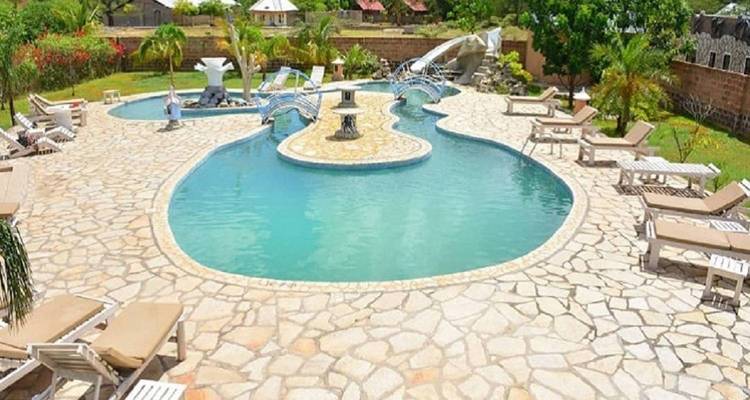 Resortpoolbereich mit Liegen und einem Springbrunnen, umgeben von einem Garten.