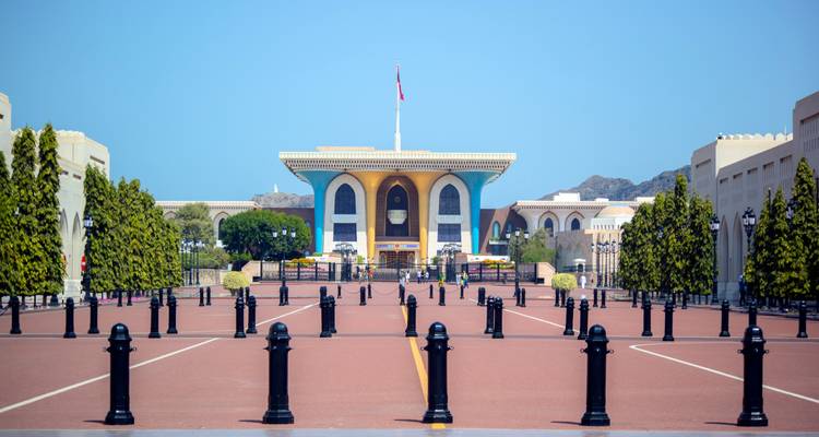 El colorido Palacio Al Alam se encuentra al final de un patio grandioso rodeado de bolardos negros y árboles bien cuidados bajo un cielo azul.