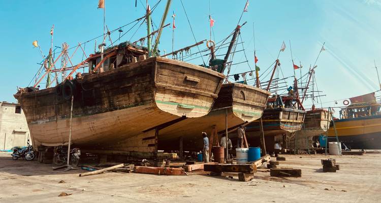 Los tradicionales dhows de madera descansan en soportes en un astillero costero mientras los trabajadores reparan sus cascos.