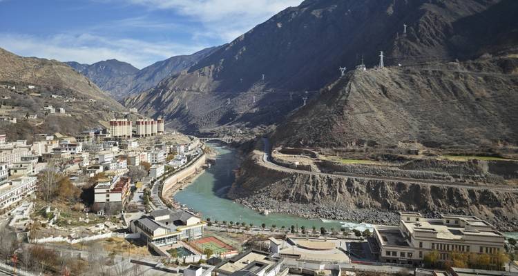 Pueblo de valle montañoso encaramado junto a un río turquesa sinuoso con laderas escarpadas y torres de teleférico.