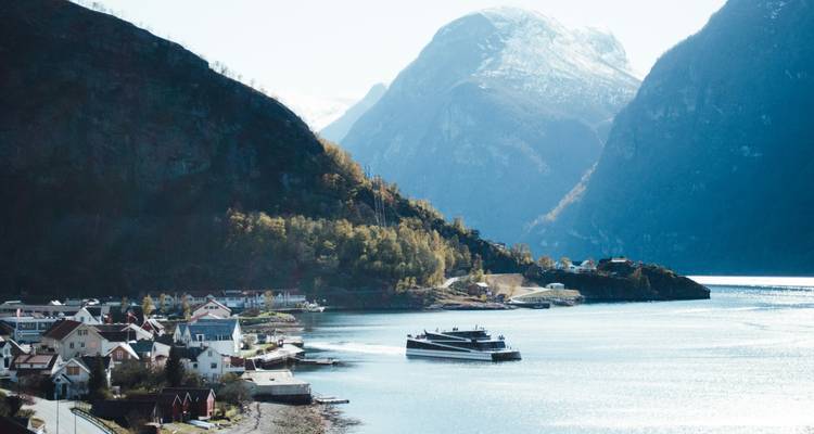 Paisaje sereno de fiordo con un moderno crucero deslizándose junto a pequeños pueblos y acantilados imponentes.