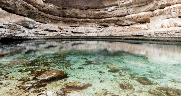 El agua turquesa cristalina llena un cenote natural de piedra caliza rodeado de paredes rocosas.