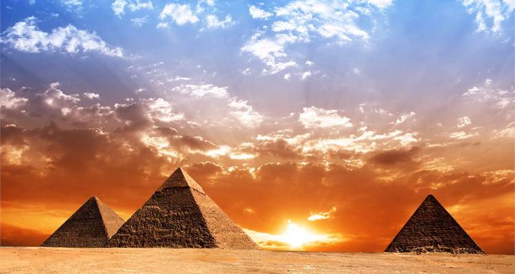 Les trois Pyramides de Giza se dressent contre un ciel de coucher de soleil dramatique avec des rayons de soleil perçant les nuages.