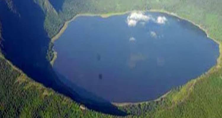 Vista aérea de un lago de cráter circular rodeado de bosque con colores apagados y baja claridad